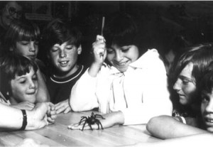 Young girl with tarantula crawling over hand while other children look on